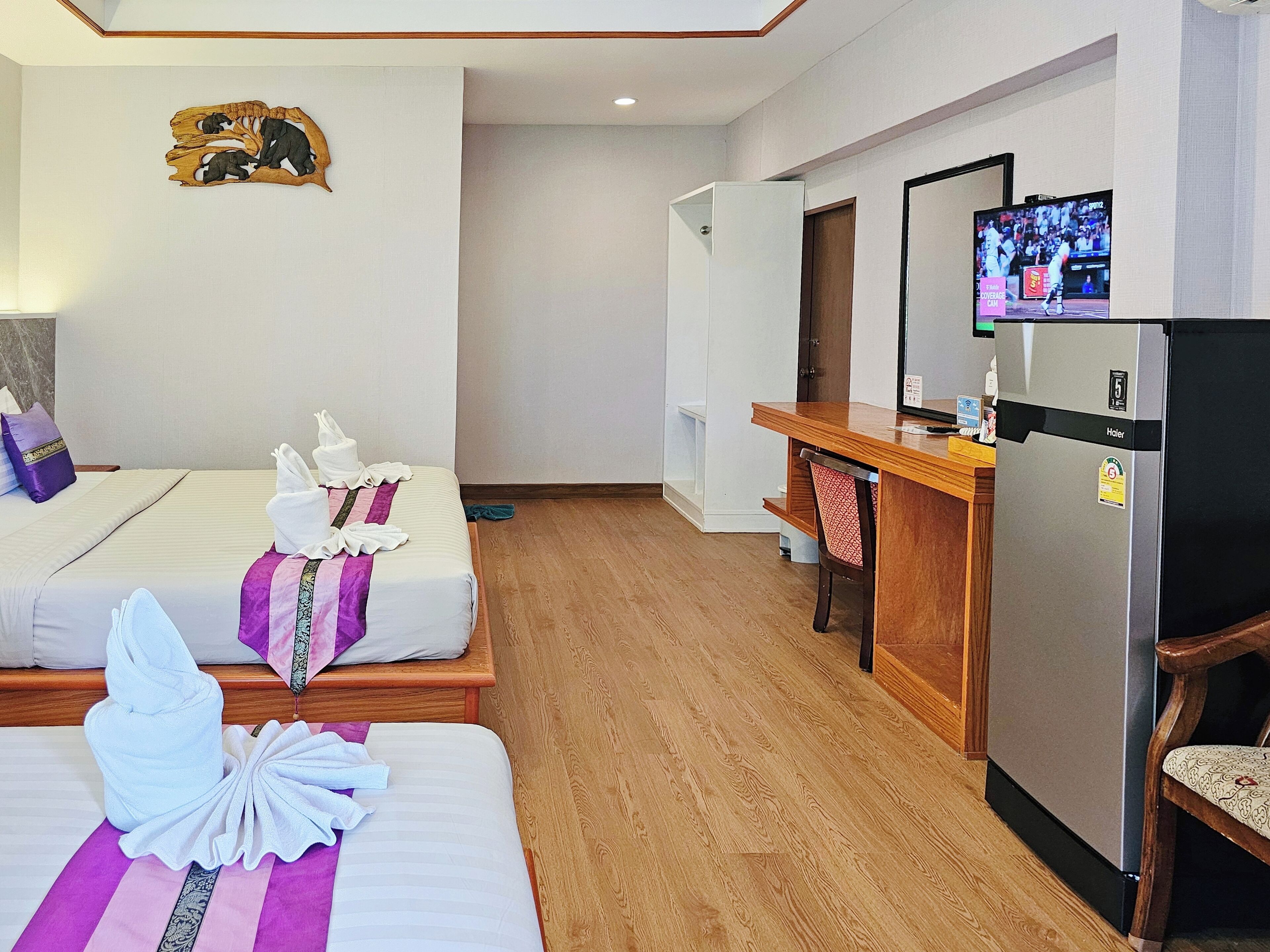 A hotel room with two beds, a wooden desk, a refrigerator, and a television.