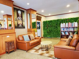 A cozy living room with leather sofas, a small round table, a bookshelf, and a green wall with plants.
