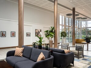 A modern lobby with a dark-colored sofa set, large potted plants, and artwork on the walls. - Hilton Garden Inn Sunderland (Sunderland)