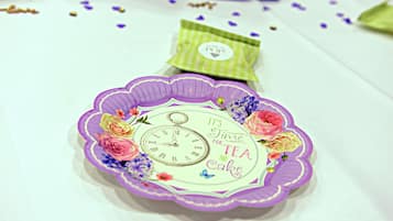 Un plato decorativo con un reloj y un diseño floral, colocado sobre una mesa con pétalos de flores dispersos.
