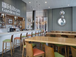 Un comedor con mesas y sillas de madera, una barra con minibar y un ventanal con cortinas.