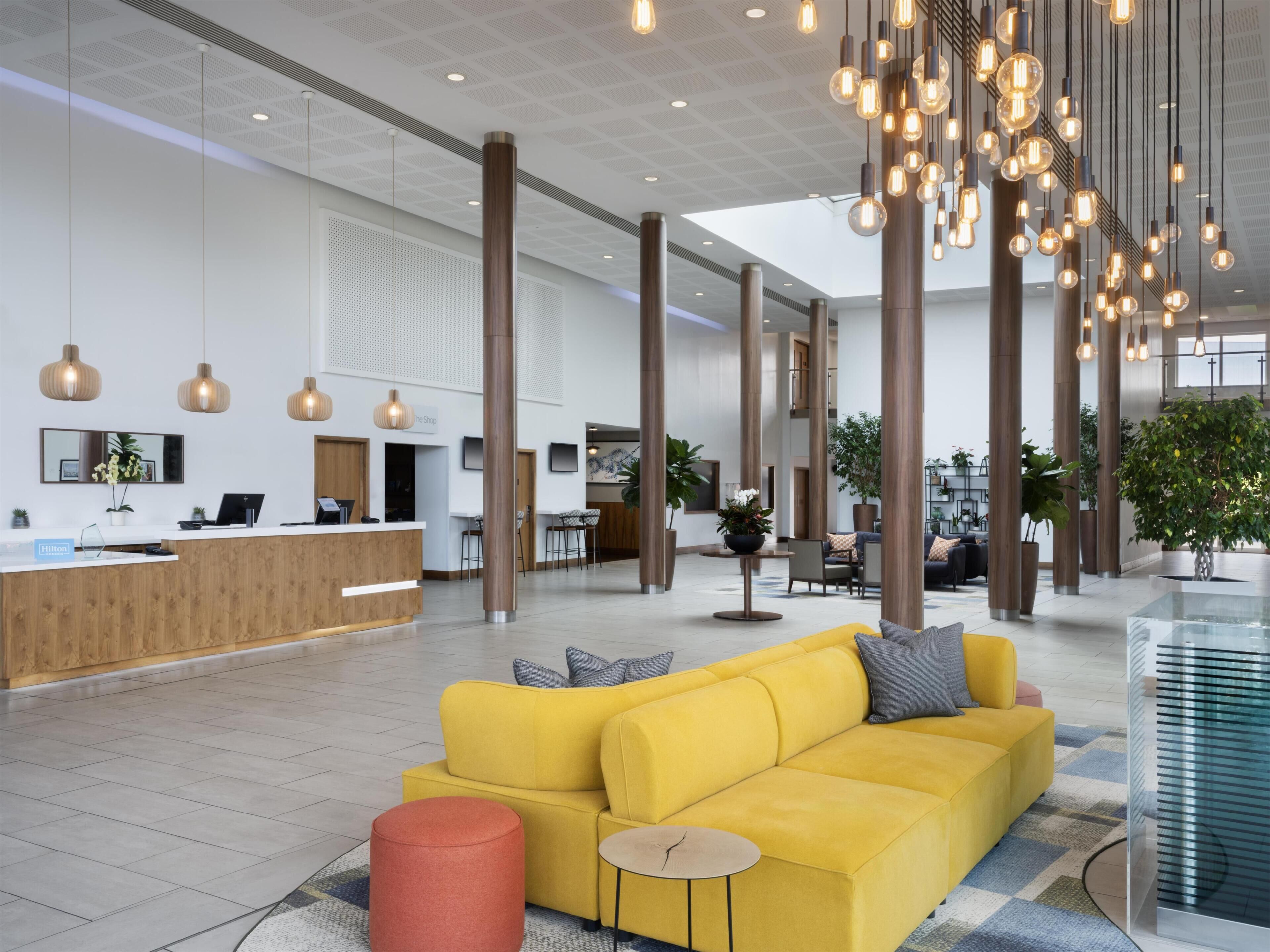 A modern hotel lobby with a reception desk, seating area, and large windows.