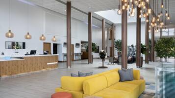 A modern hotel lobby with a reception desk, seating area, and large windows.