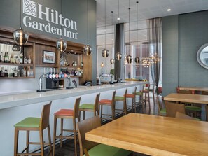 Eine Bar mit Minibar, Barhocker und einer Sitzecke mit Tischen und Stühlen.
