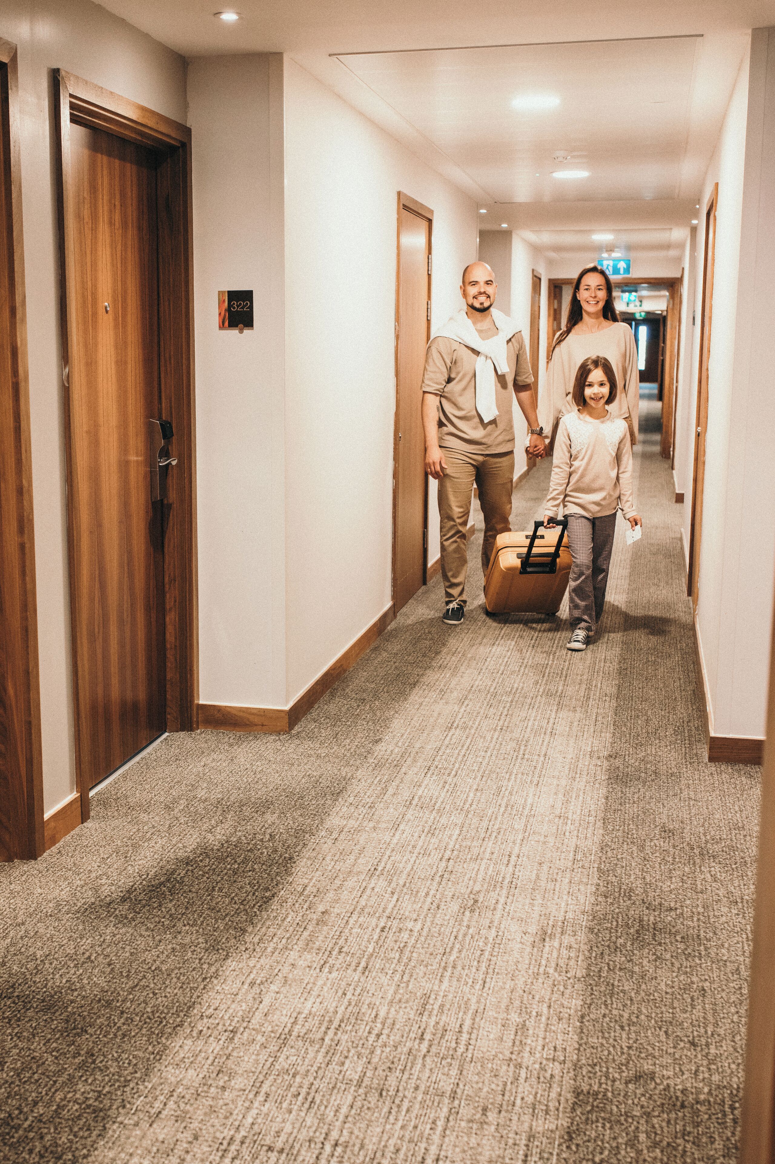 En hotellkorridor med trädörrar, heltäckningsmatta på golvet och en skylt som visar att det är rum nummer 322.