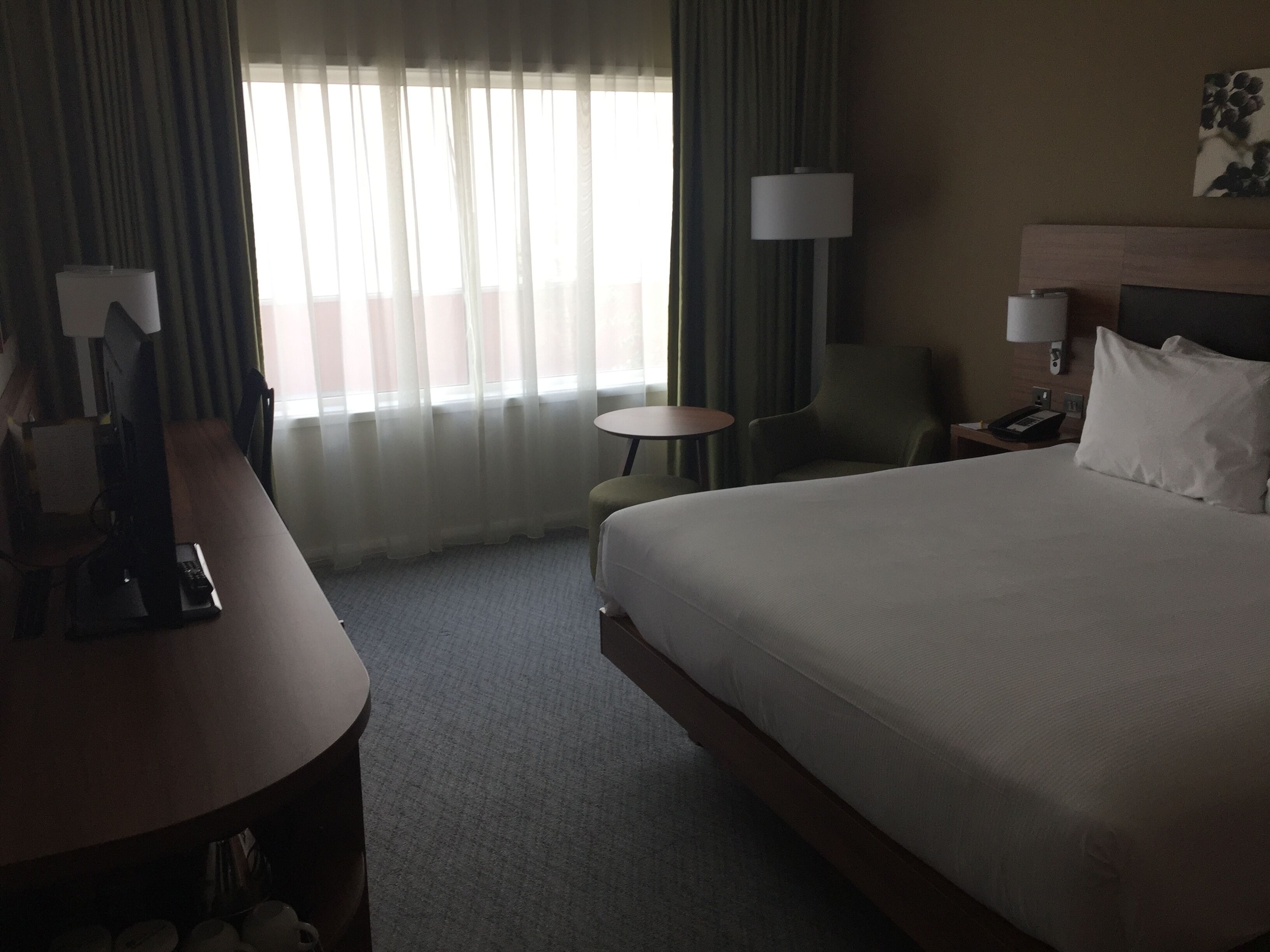 A hotel room with a large bed, two bedside tables, a desk, a chair, and a small round table.