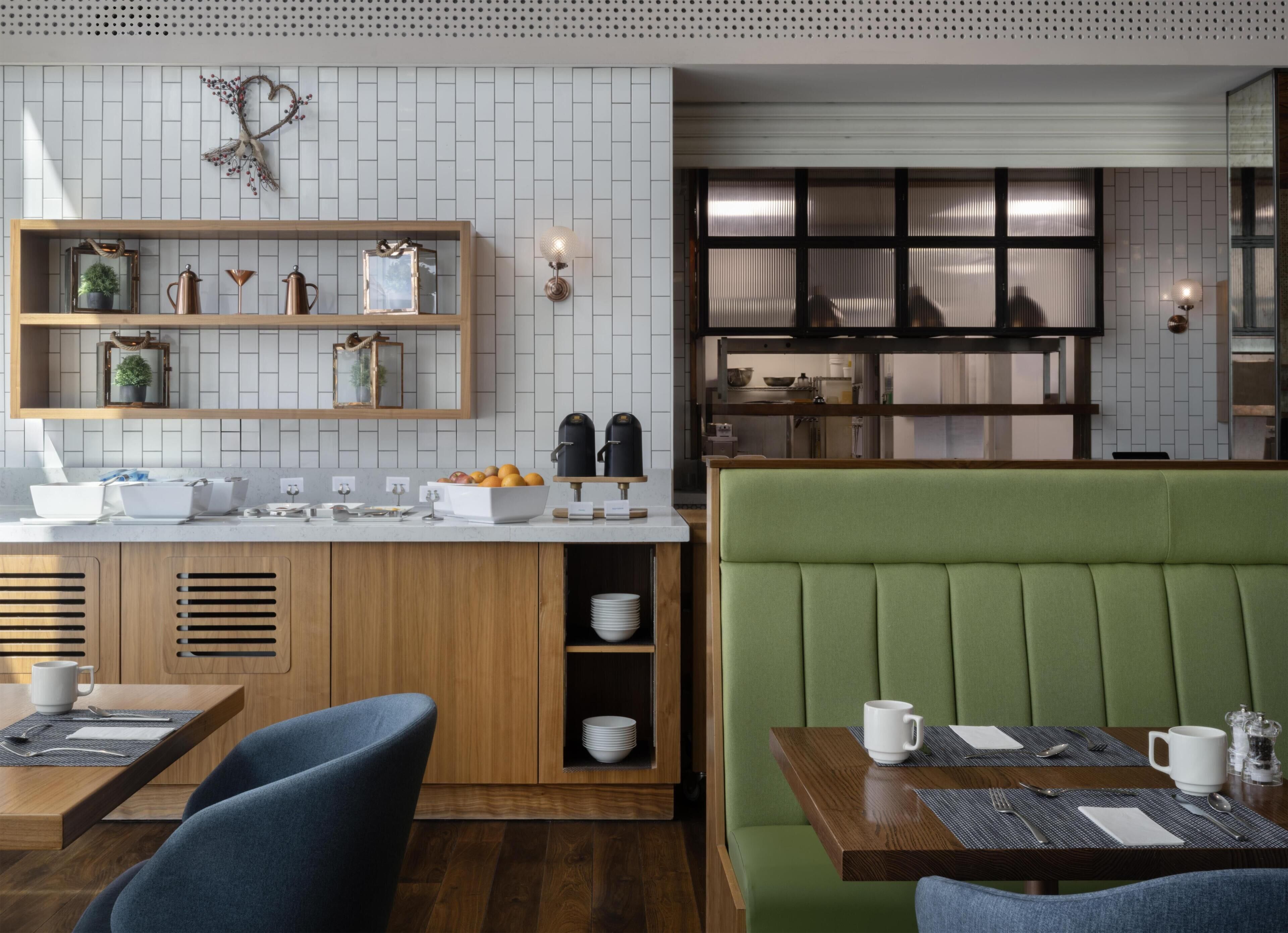 A modern restaurant with a wooden counter, green booth seating, and a tiled backsplash.