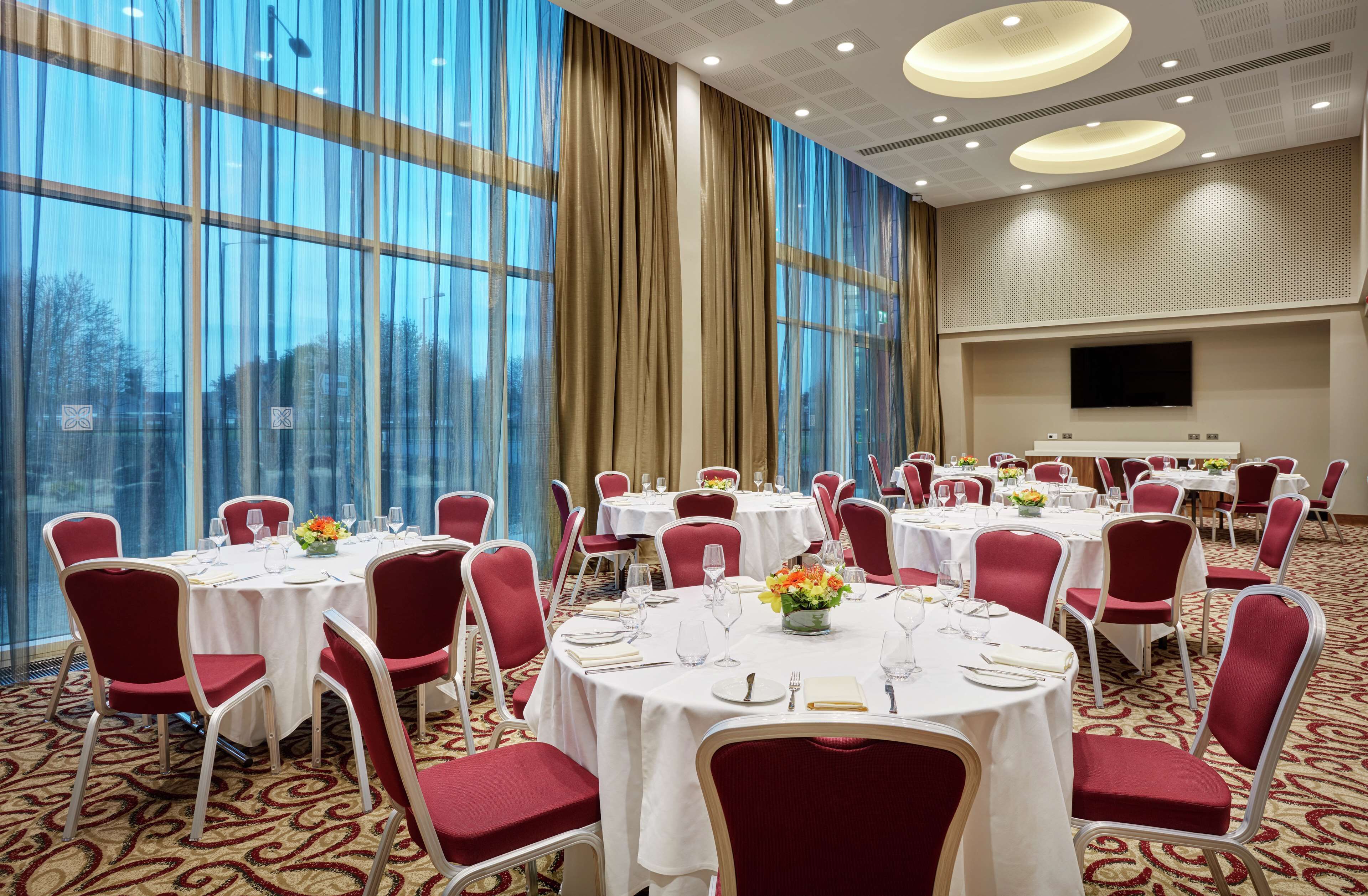 A banquet hall with round tables, red chairs, and white tablecloths.