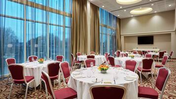 A banquet hall with round tables, red chairs, and white tablecloths.