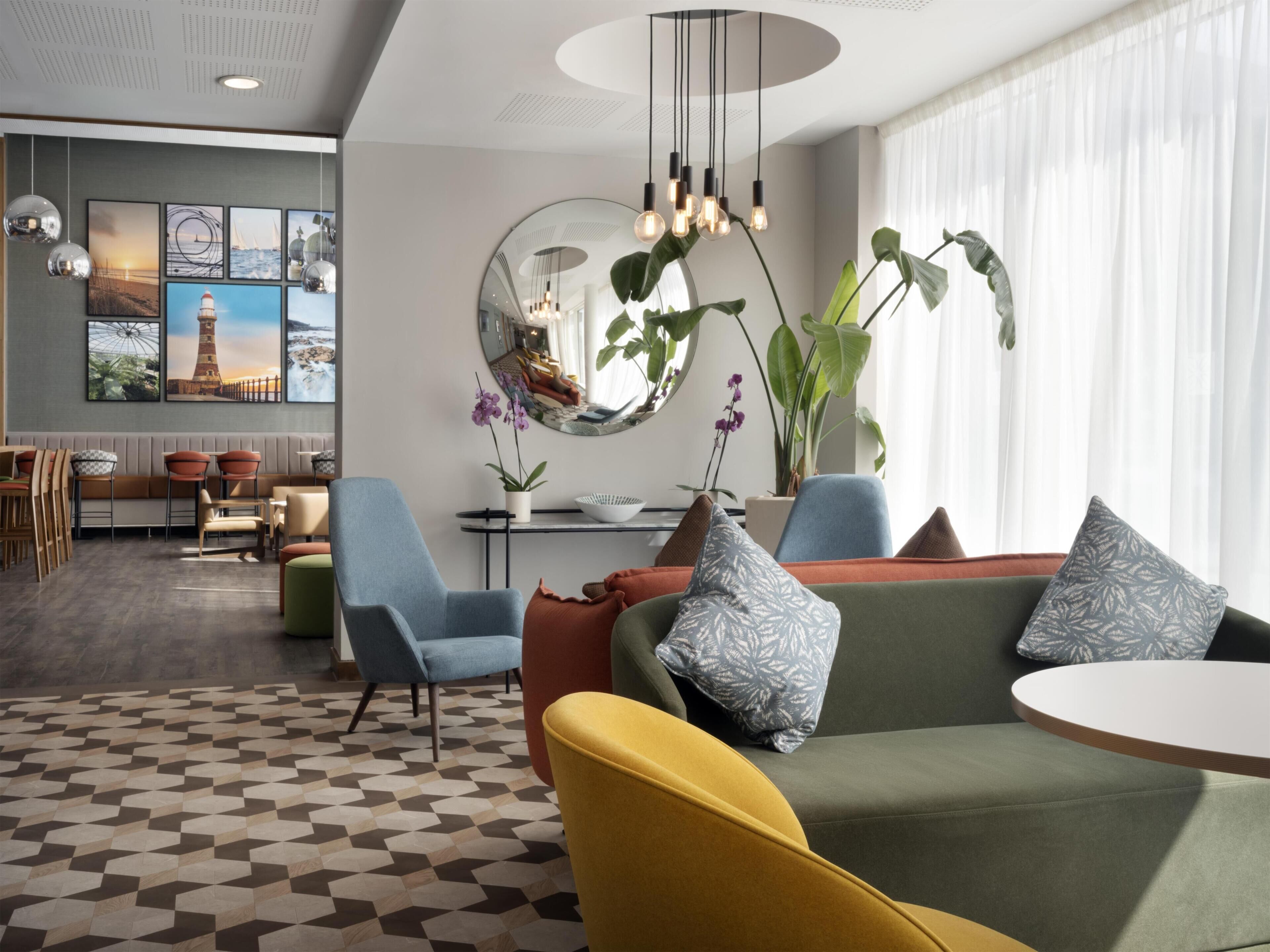 A modern lounge area with seating, a patterned floor, and a large mirror reflecting the room.