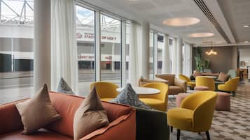 A modern hotel lobby with large windows, yellow and orange seating, and a view of the outside.