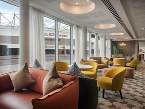 Un moderno vestíbulo de hotel con grandes ventanales, asientos amarillos y anaranjados, y vistas al exterior.