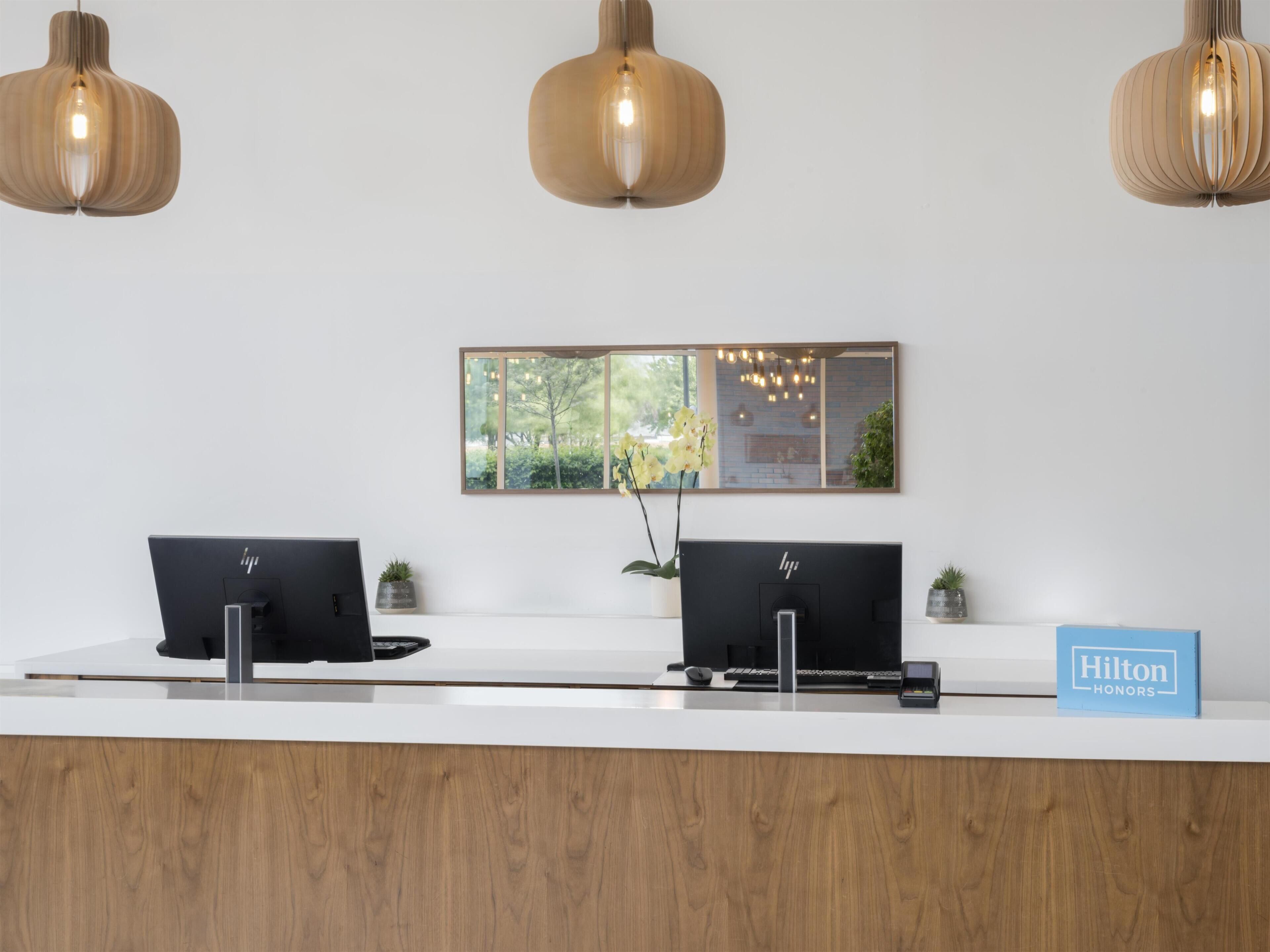 A hotel reception desk with two HP computers, a mirror reflecting the outdoors, and a Hilton Honors sign.