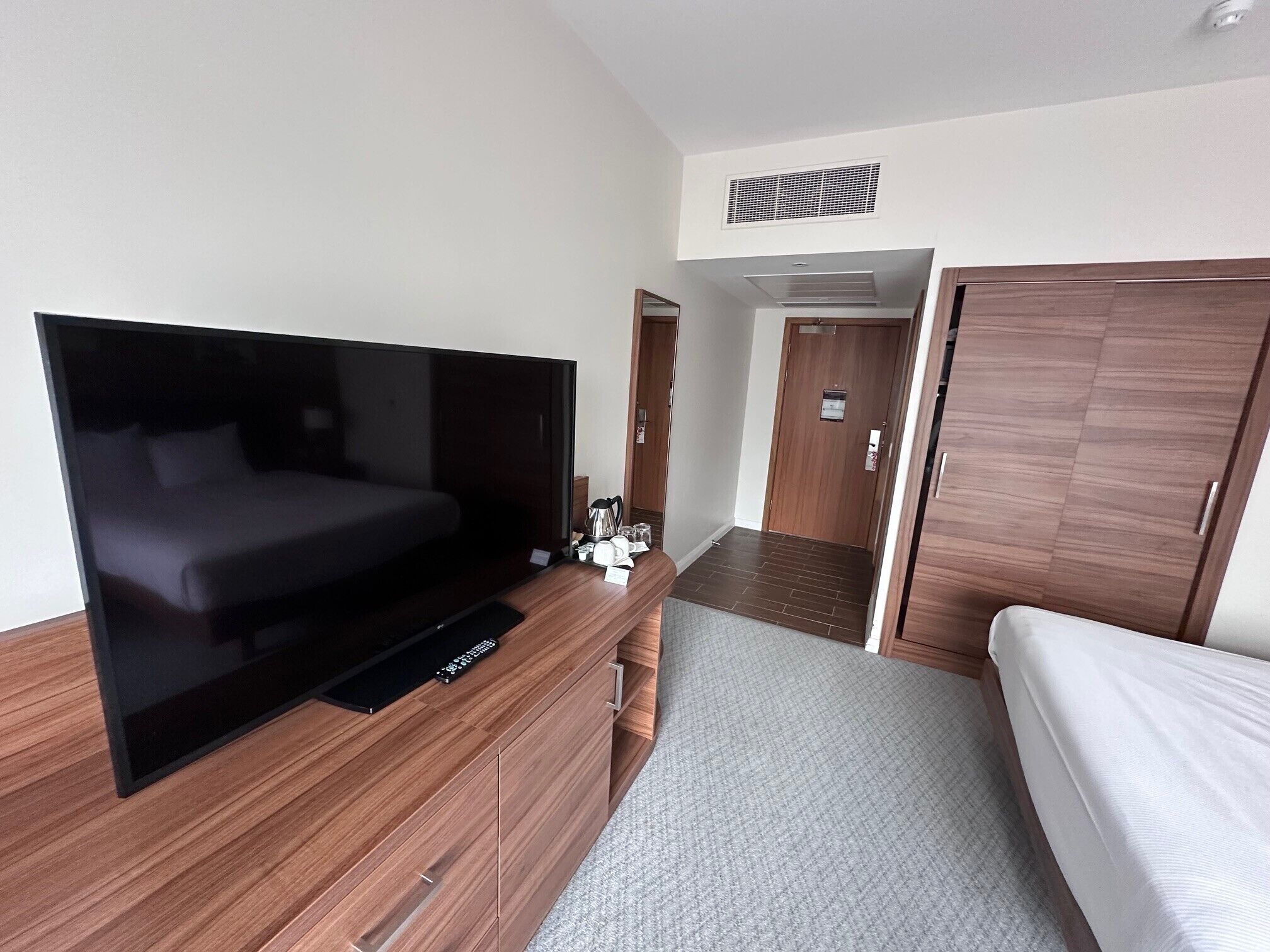 Ein modernes Hotelzimmer mit einem großen Flachbildfernseher, einem Bett, einer Holzkommode und einem Kleiderschrank.
