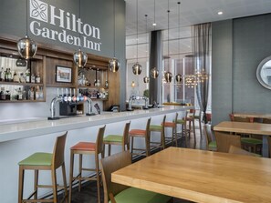 A bar area with a minibar, bar stools, and a seating area with tables and chairs. - Hilton Garden Inn Sunderland (Sunderland)