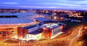 A stadium with a large, curved roof and adjacent buildings with illuminated windows and signage. - Hilton Garden Inn Sunderland (Sunderland)