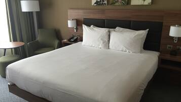 A hotel room with a large bed, two bedside lamps, a telephone, a chair, and artwork on the wall.