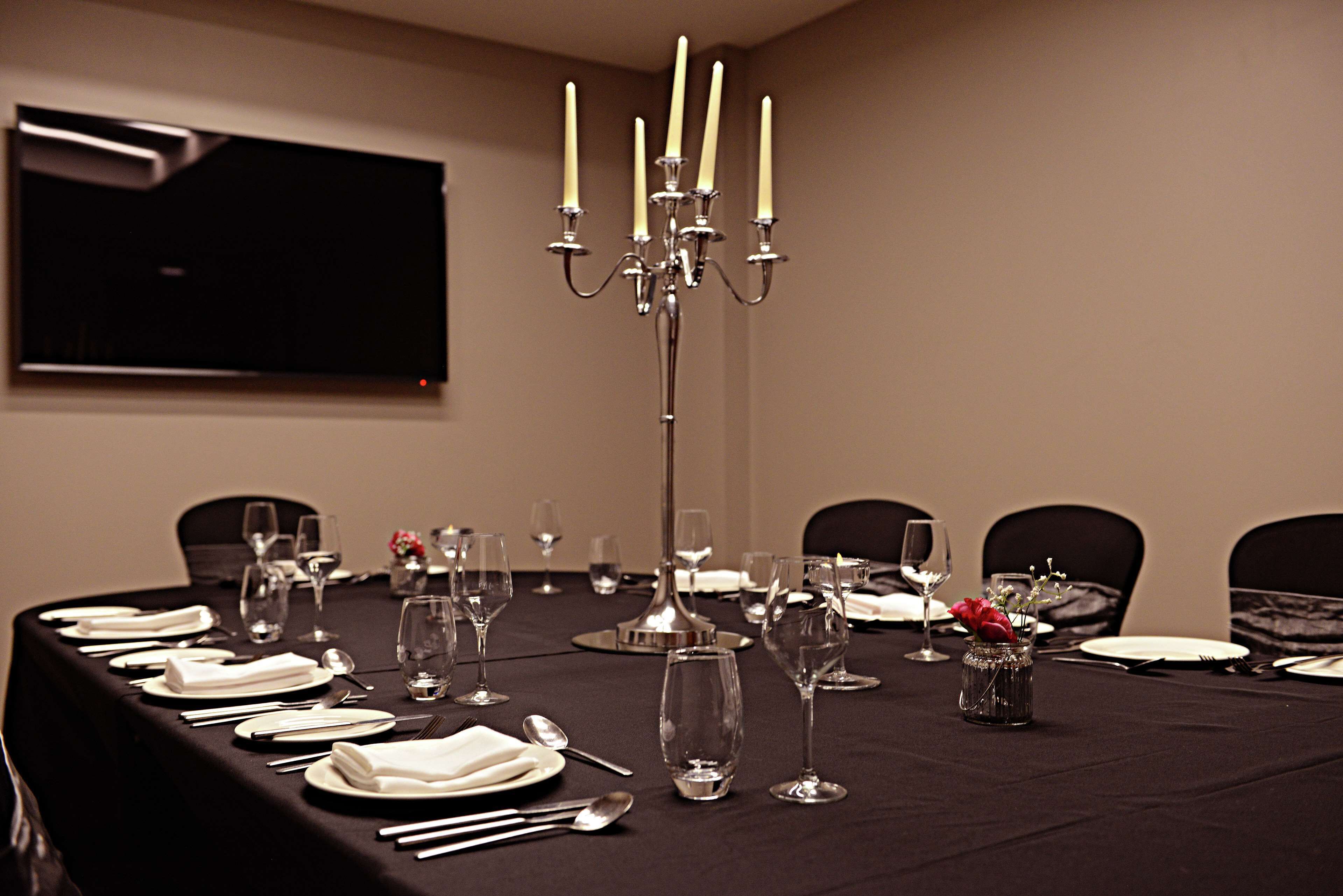 Une salle de conférence avec une longue table dressée pour un événement officiel, un chandelier et un téléviseur fixé au mur.