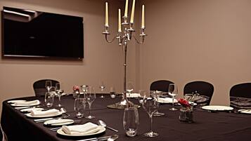 Une salle de conférence avec une longue table dressée pour un événement officiel, un chandelier et un téléviseur fixé au mur.
