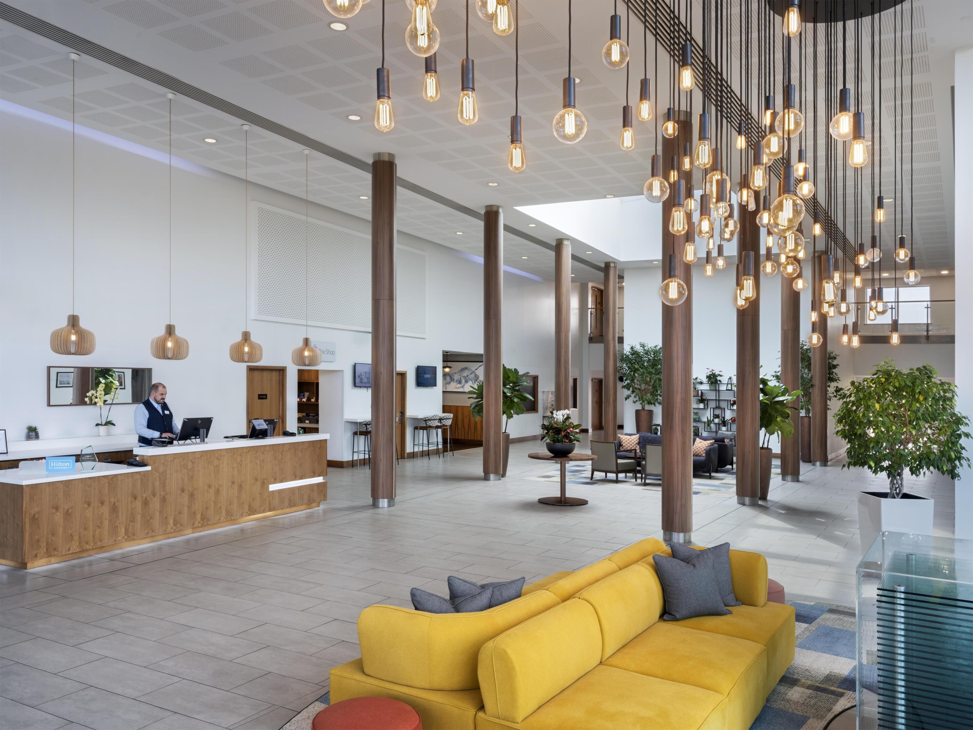 Um saguão de hotel com balcão de recepção, área de estar e luminárias modernas.