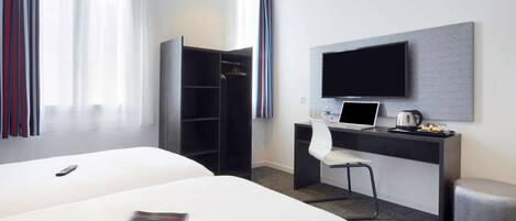 A hotel room with a large bed, a desk with a laptop, a TV, and a wardrobe.