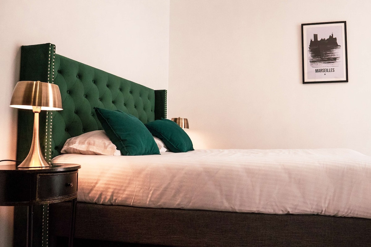 A neatly made bed with a green headboard, a bedside lamp, and a framed picture of a cityscape on the wall.
