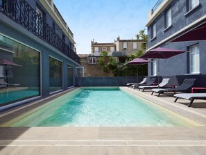 A swimming pool with lounge chairs and umbrellas, surrounded by buildings with balconies and large windows. - Kyriad Marseille Blancarde - Timone (Marseille)