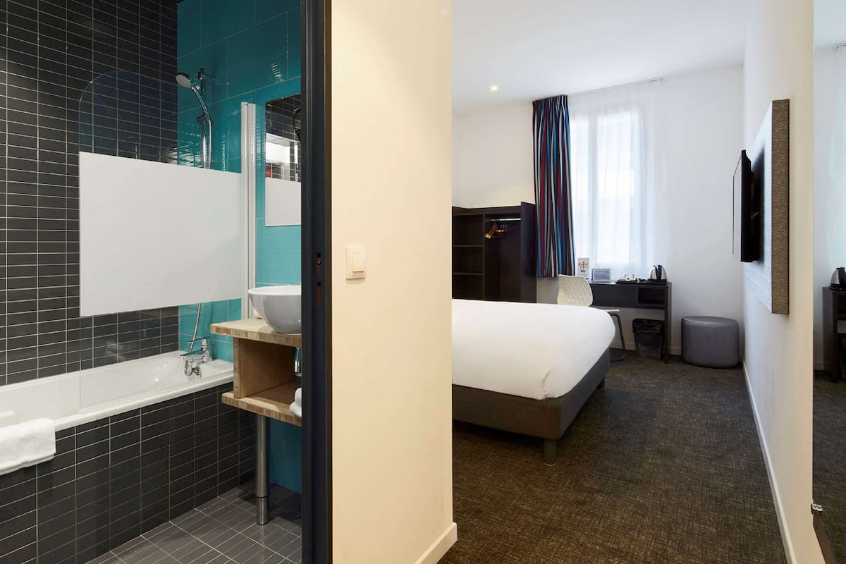 A modern hotel room with a large bed, a separate bathroom with a bathtub, and a desk with a chair.