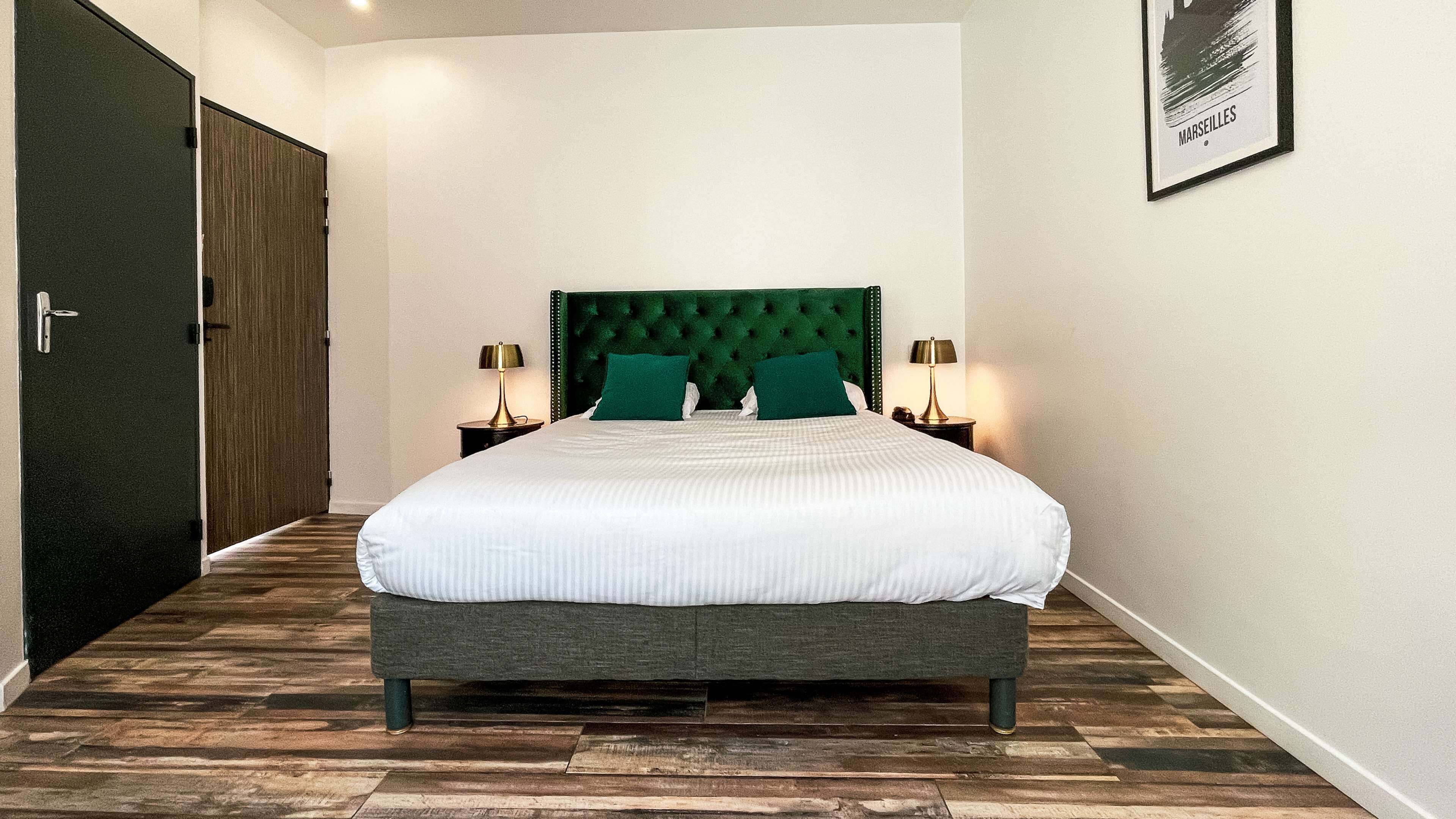 Habitación de hotel con una cama grande, cabecera verde, dos mesitas de noche con lámparas y un cuadro en la pared.