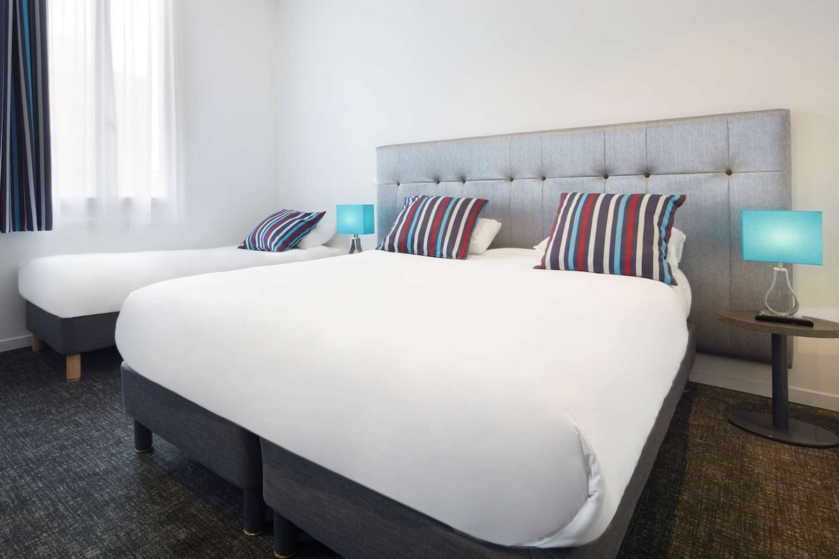A hotel room with a large bed, two bedside tables, a window with curtains, and a carpeted floor.