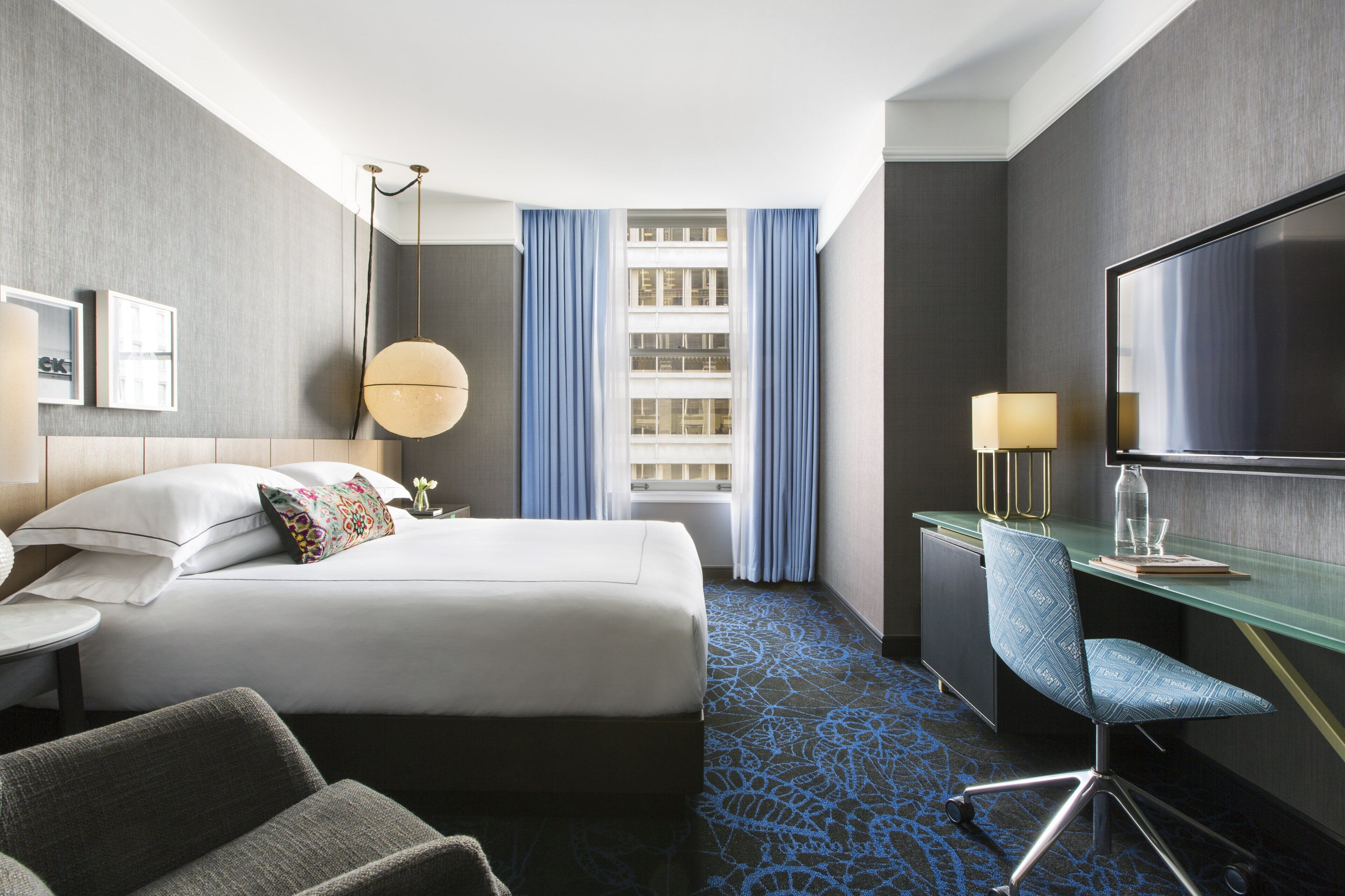 Une chambre d’hôtel équipée d’un lit, d’un bureau, d’une chaise, d’une télévision et d’une fenêtre avec des rideaux.