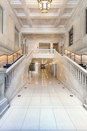 A grand hallway with marble floors and a central staircase with a balustrade. - Kimpton Gray Hotel by IHG (Chicago)