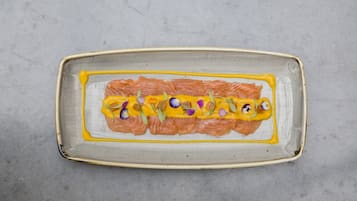 A rectangular ceramic plate with salmon and yellow sauce, garnished with purple flowers.