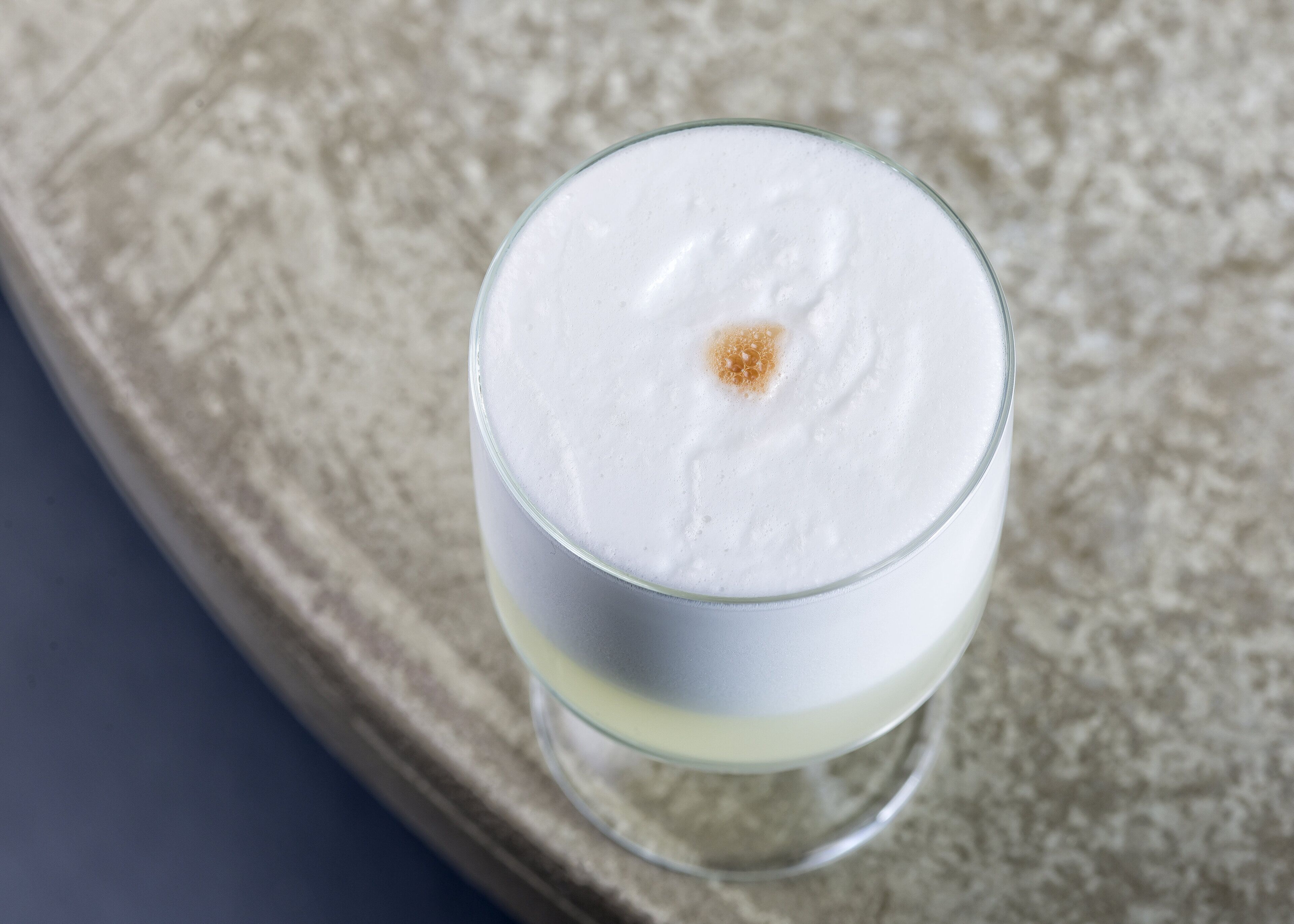 Un verre contenant une boisson blanche et surmontée d’une mousse, posé sur une surface texturée.