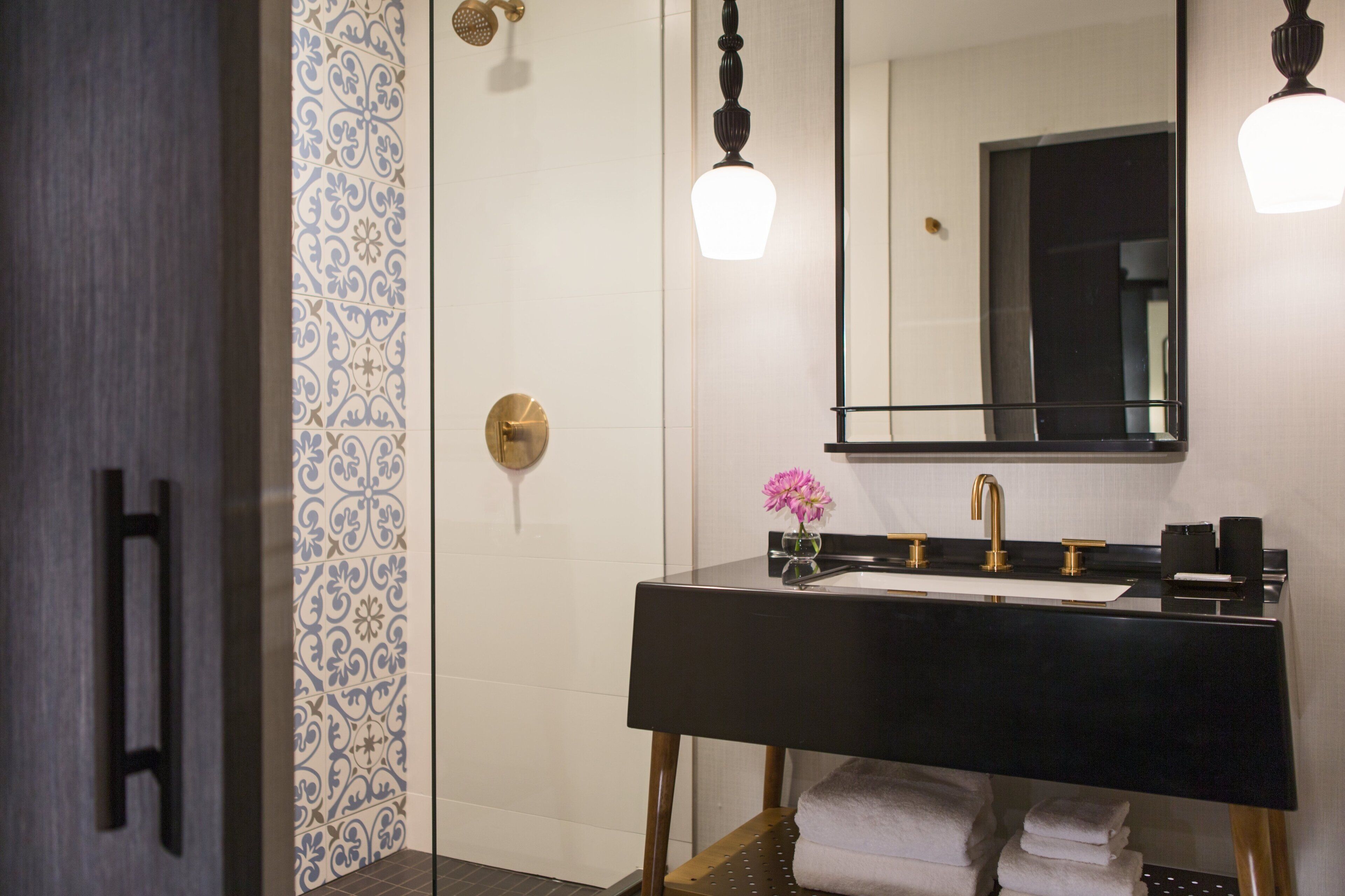 Une salle de bain avec un lavabo noir, des robinetteries dorées et un mur de douche orné d’un motif.