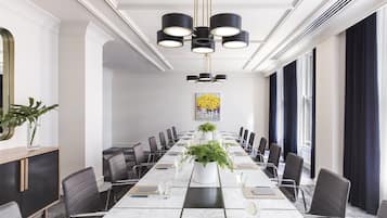 A conference room with a long table, chairs, a potted plant, and a chandelier.