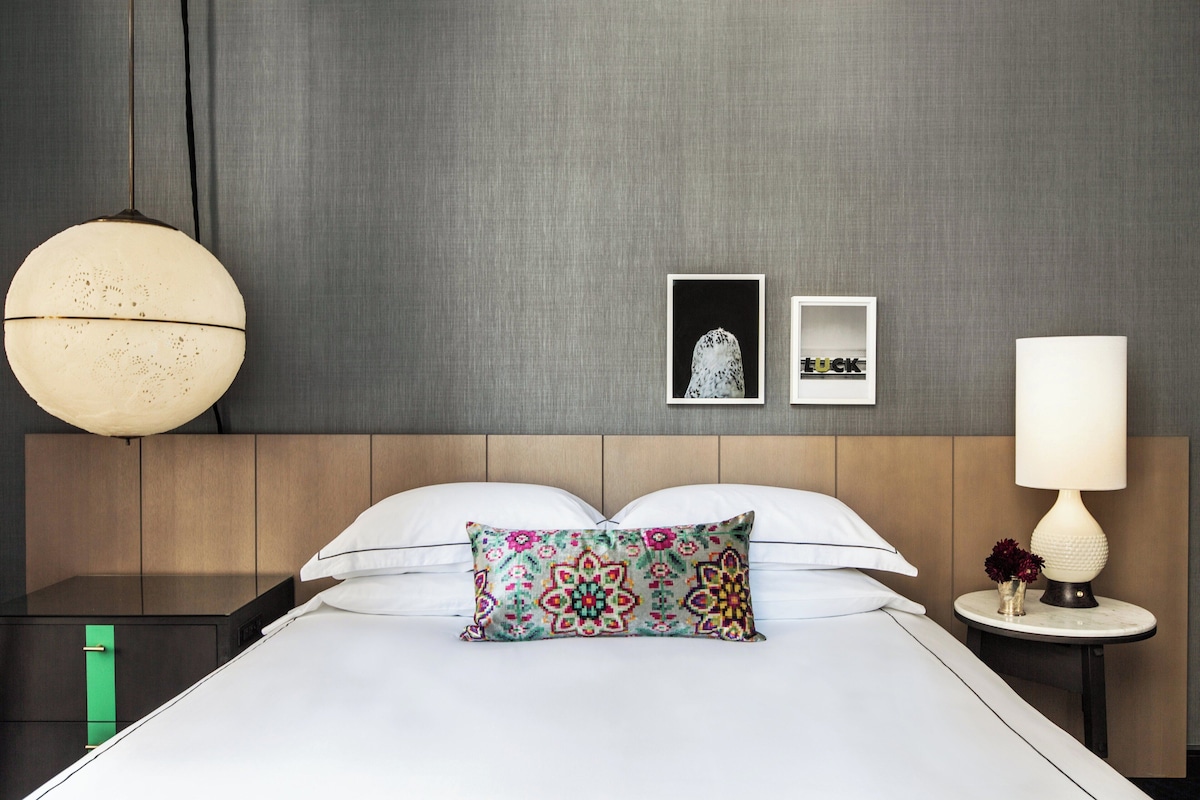 Une chambre d’hôtel avec un lit, une table de chevet, une lampe et un mur orné de deux tableaux encadrés.