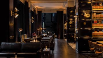 A dimly lit interior with leather seating, tables, and a bookshelf filled with books.