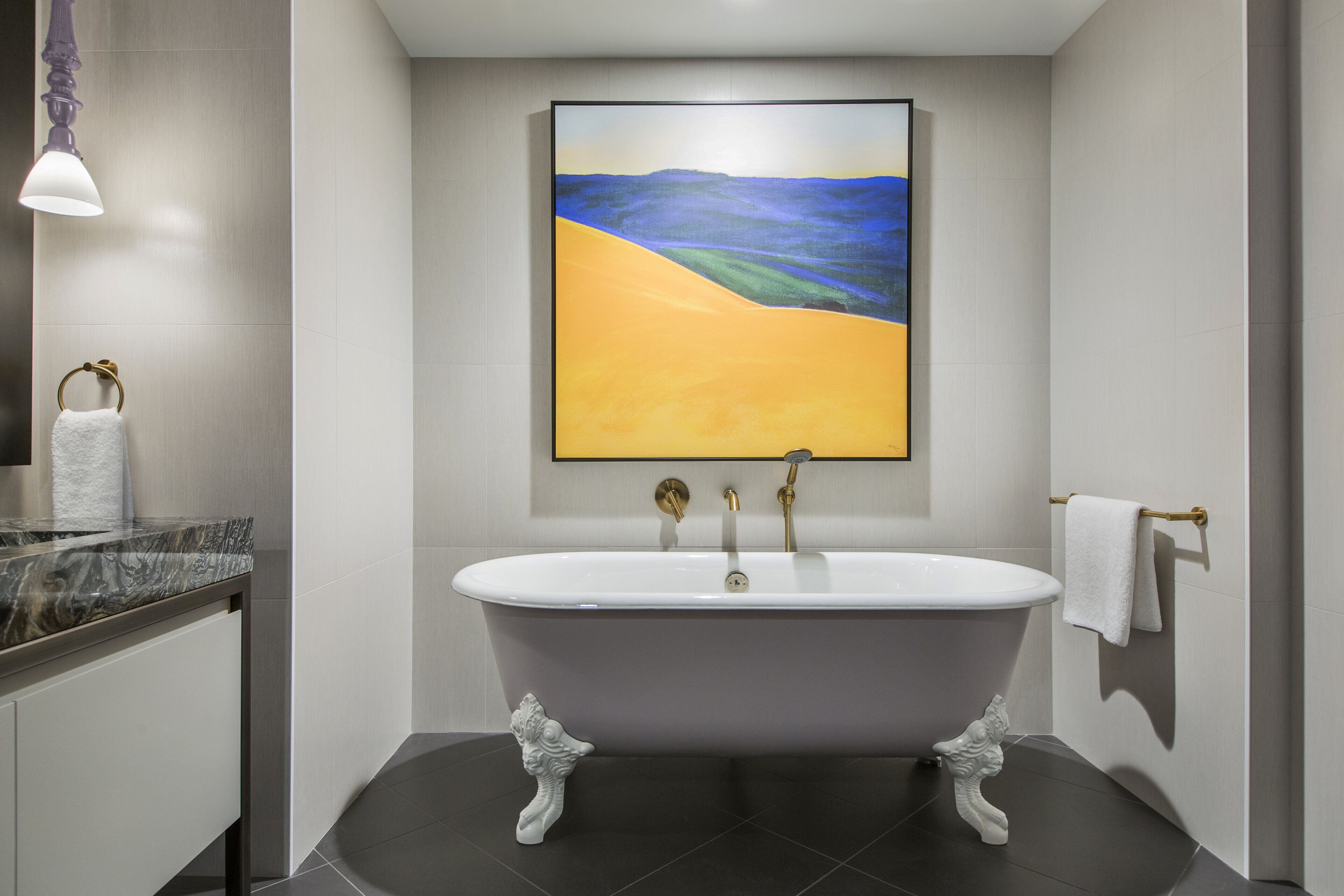 A modern bathroom with a freestanding bathtub, a marble countertop, and a large abstract painting on the wall.