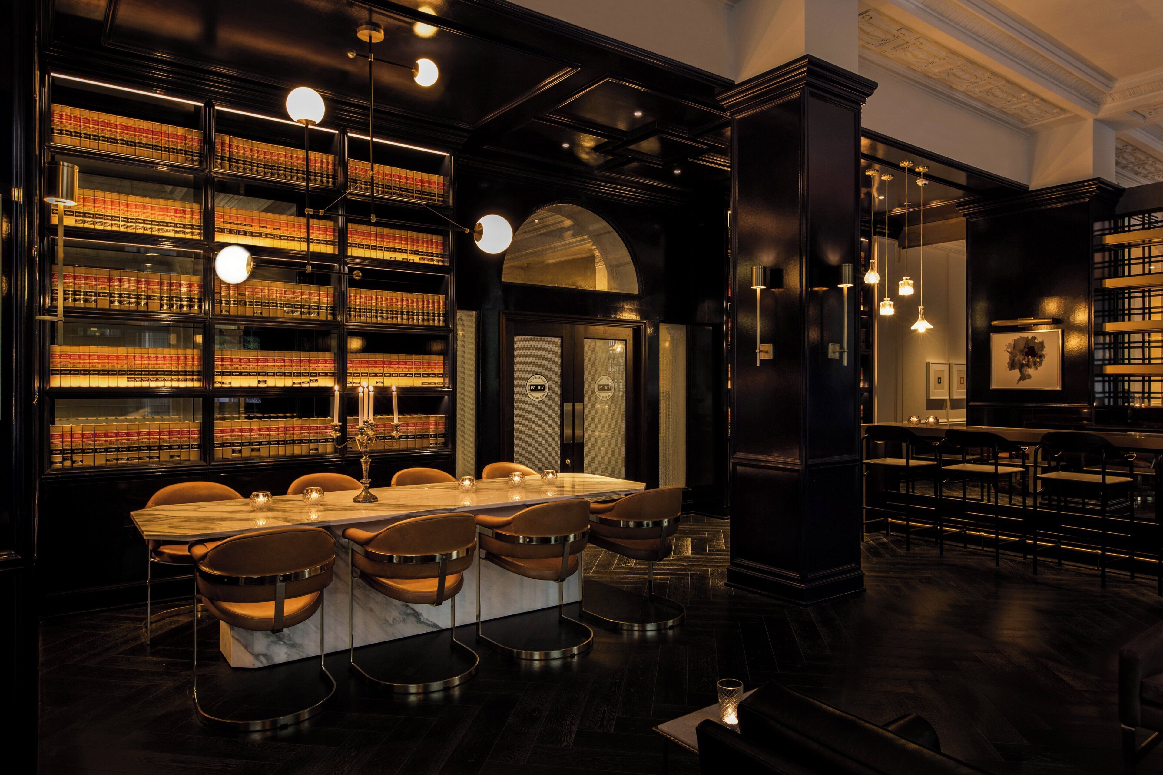 A library with bookshelves, a marble table, and bar stools.