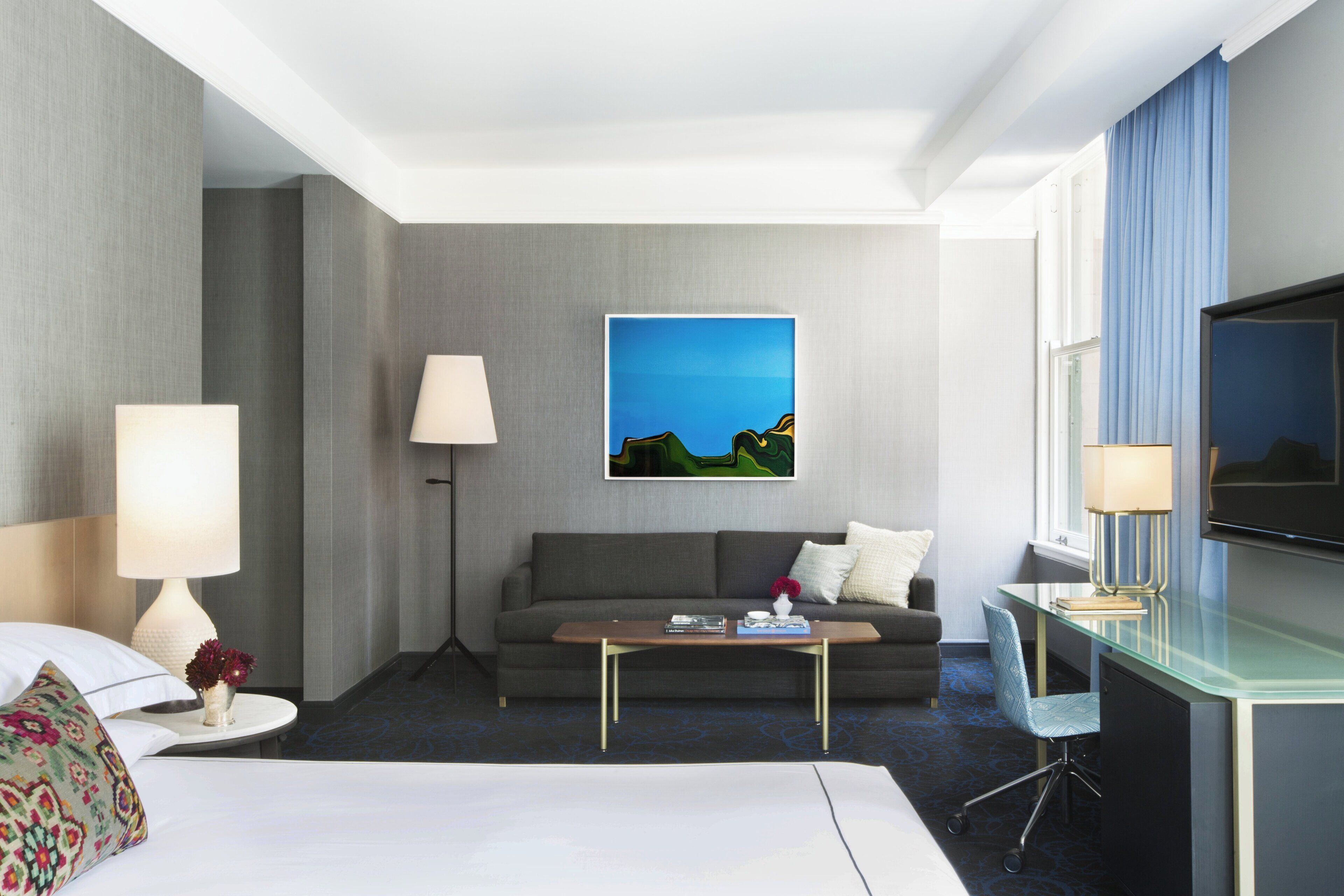 Une chambre d’hôtel avec un lit, un canapé, une table basse, une télévision et un tableau au mur.