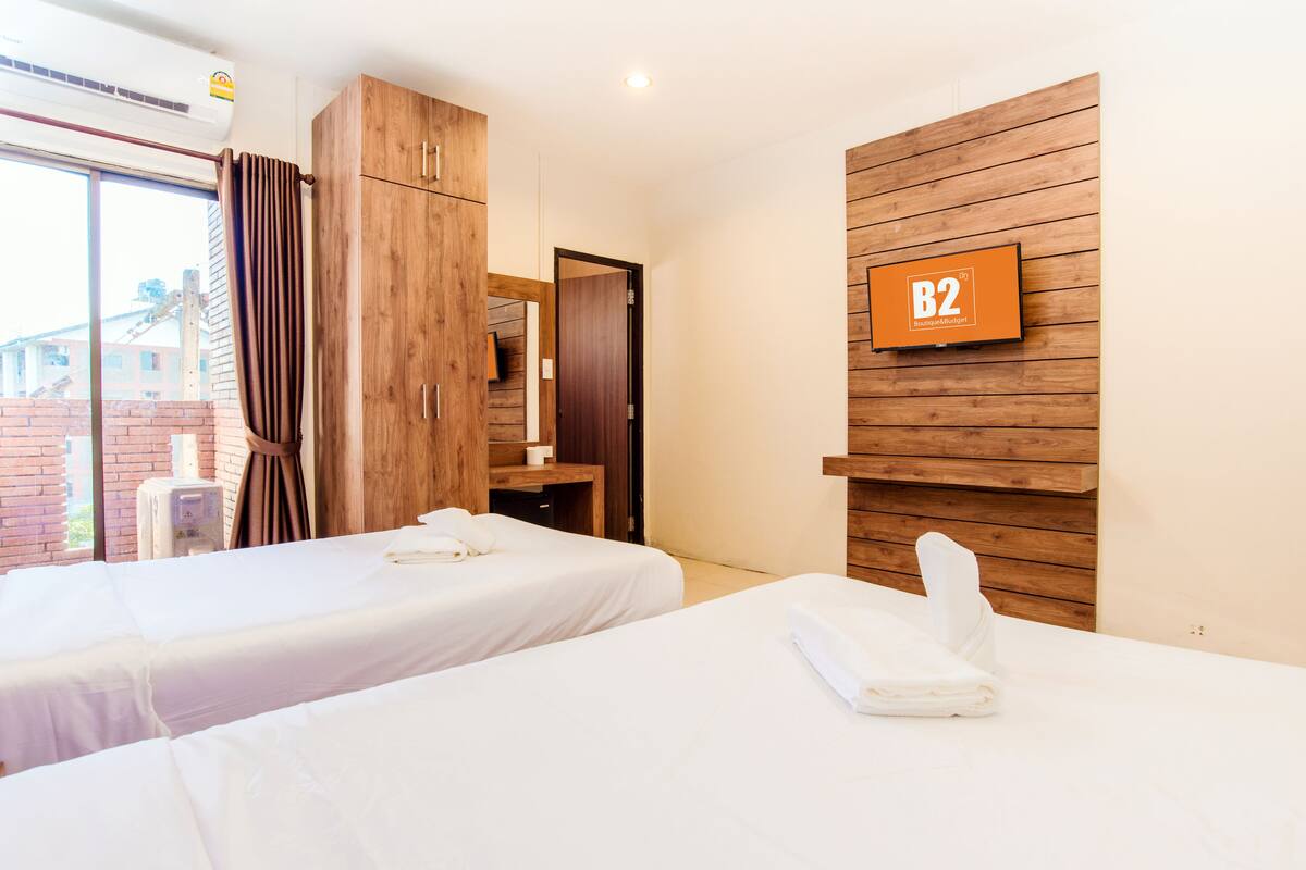 Ein Hotelzimmer mit zwei Betten, Holzvertäfelung, einem an der Wand montierten Fernseher und einer sichtbaren Badezimmertür.
