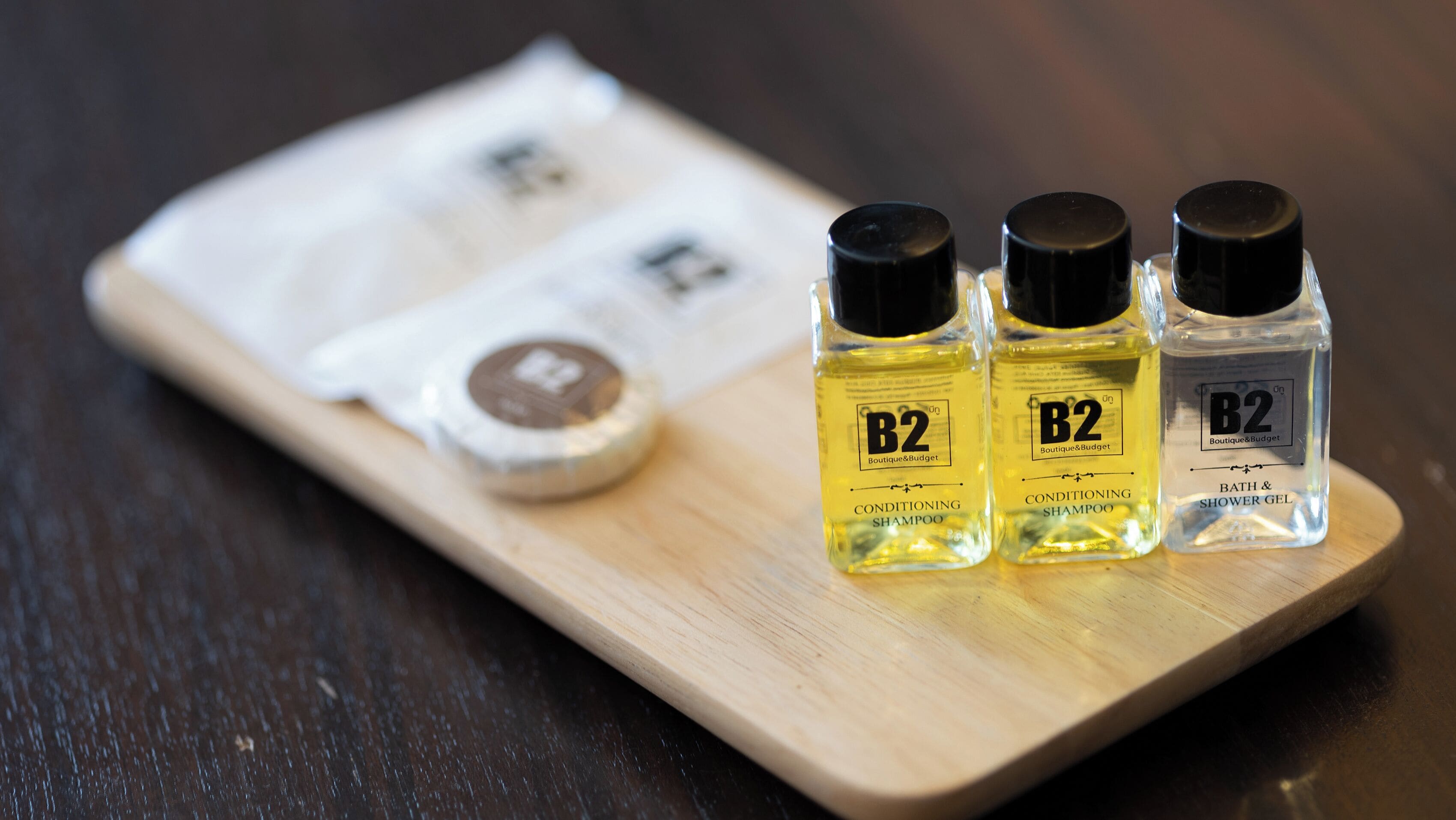 Tres botellas de champú acondicionador B2 y un pequeño envase de gel de baño y ducha B2 sobre una bandeja de madera.