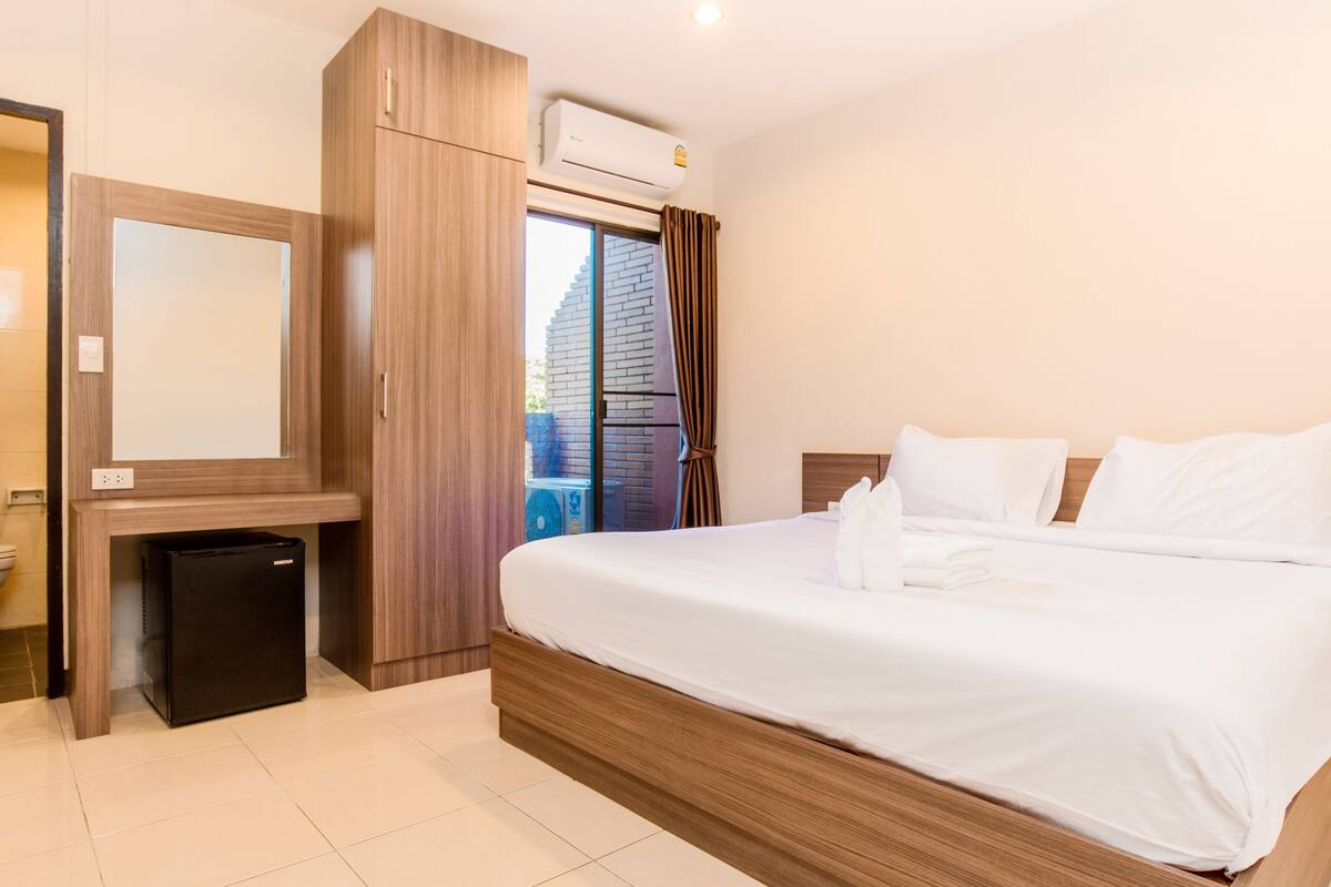 Ein modernes Hotelzimmer mit einem hölzernen Bett, einem kleinen Schreibtisch, einem Spiegel und Blick ins Freie.