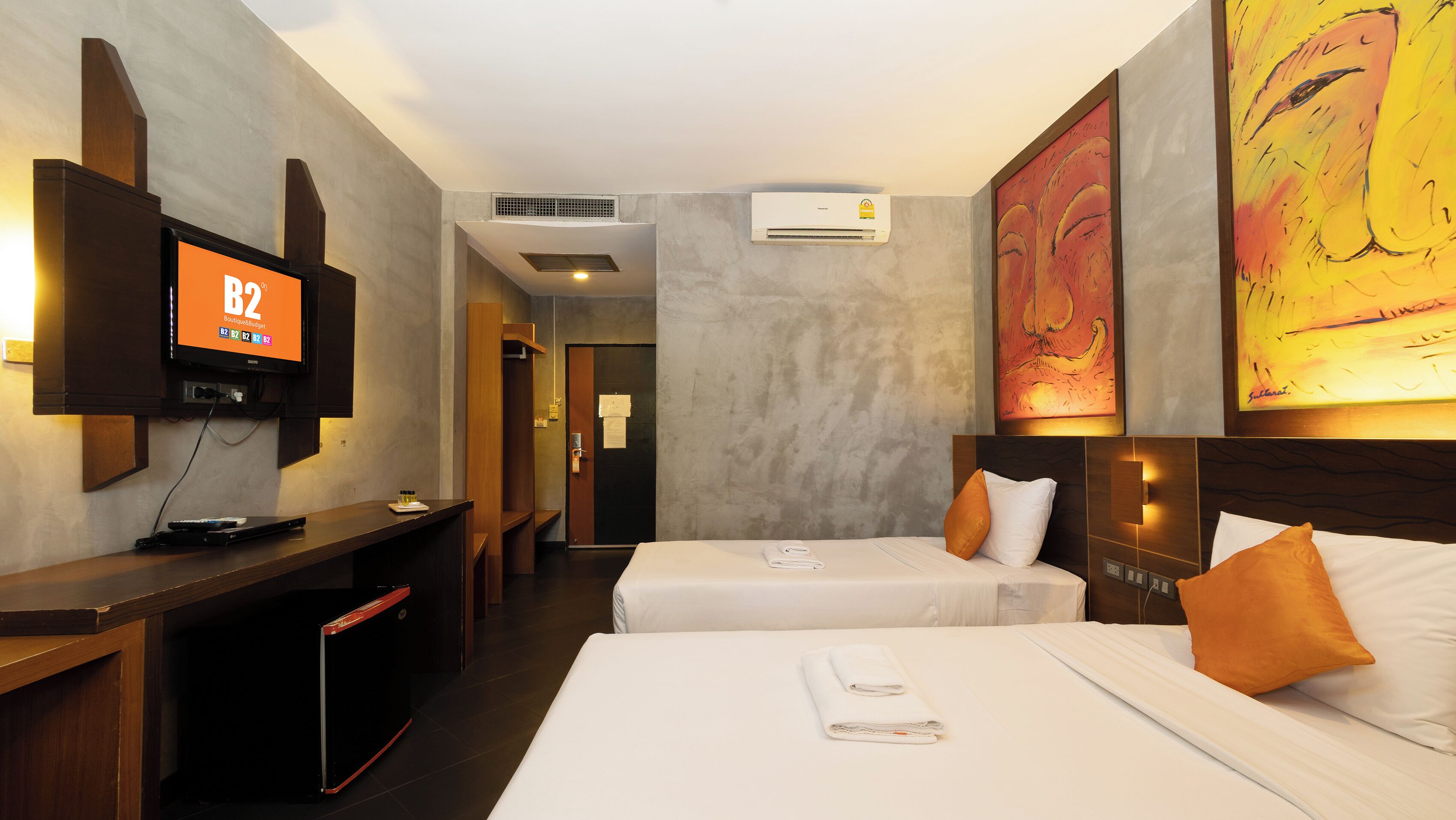 Ein Hotelzimmer mit zwei Betten, einem Fernseher und Bildern an den Wänden.