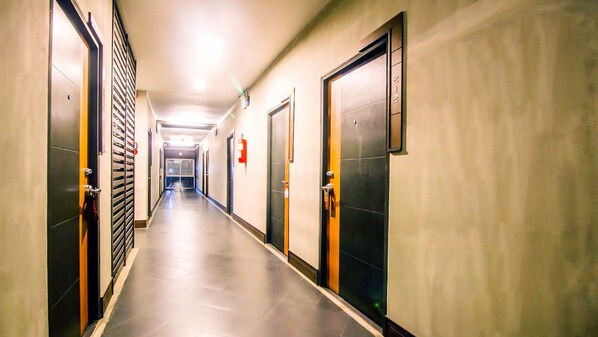 Un pasillo largo y estrecho de hotel con puertas a ambos lados, un extintor en la pared y una luz en el techo.