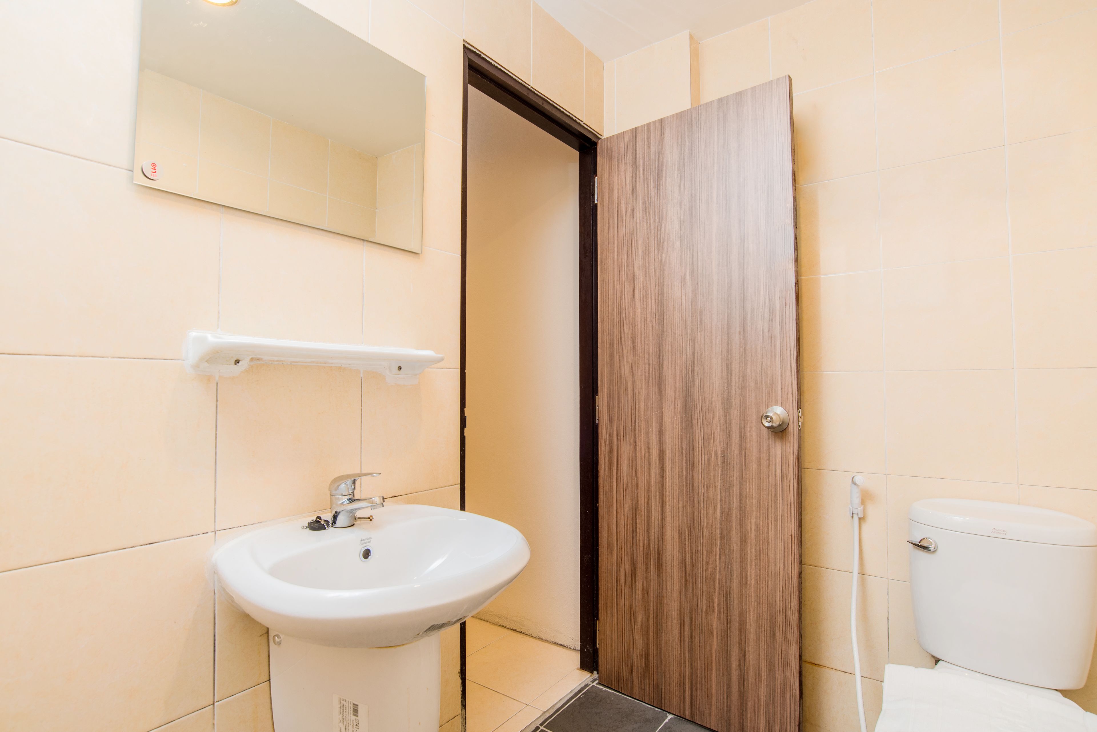 A bathroom with a white sink, a mirror, a wooden door, and a toilet.