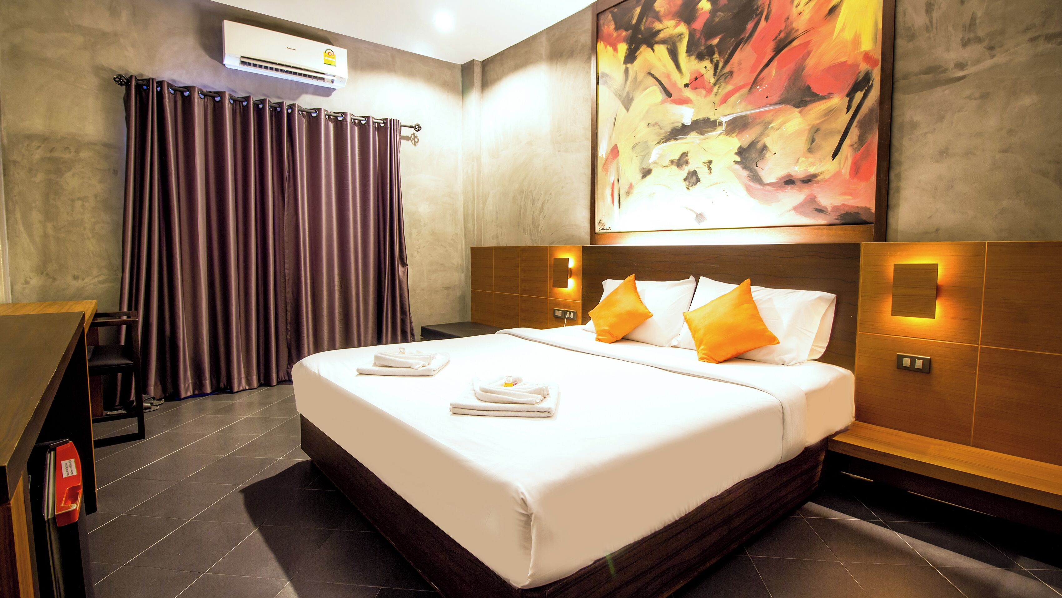 A hotel room with a large bed, a desk, and a painting on the wall.