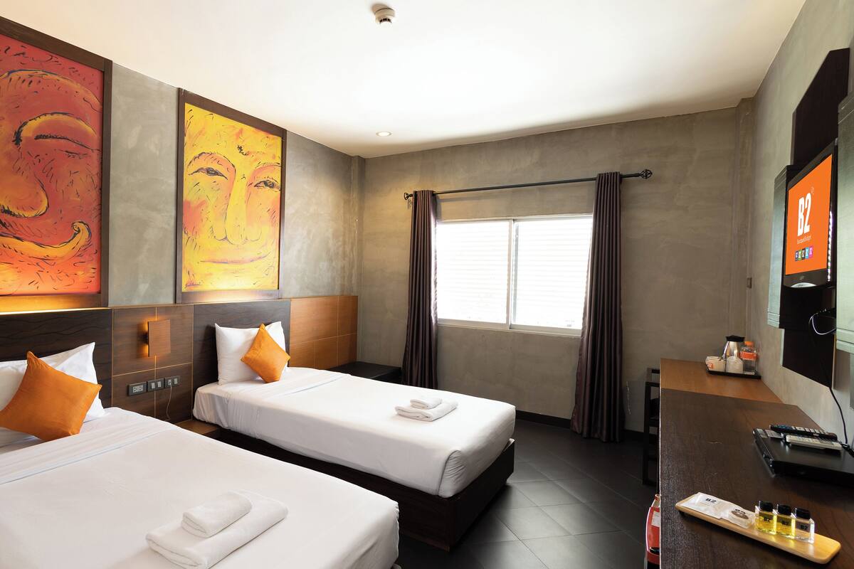 Ein Hotelzimmer mit zwei Betten, einem Fernseher, einem Schreibtisch mit Computer und Bildern an den Wänden.