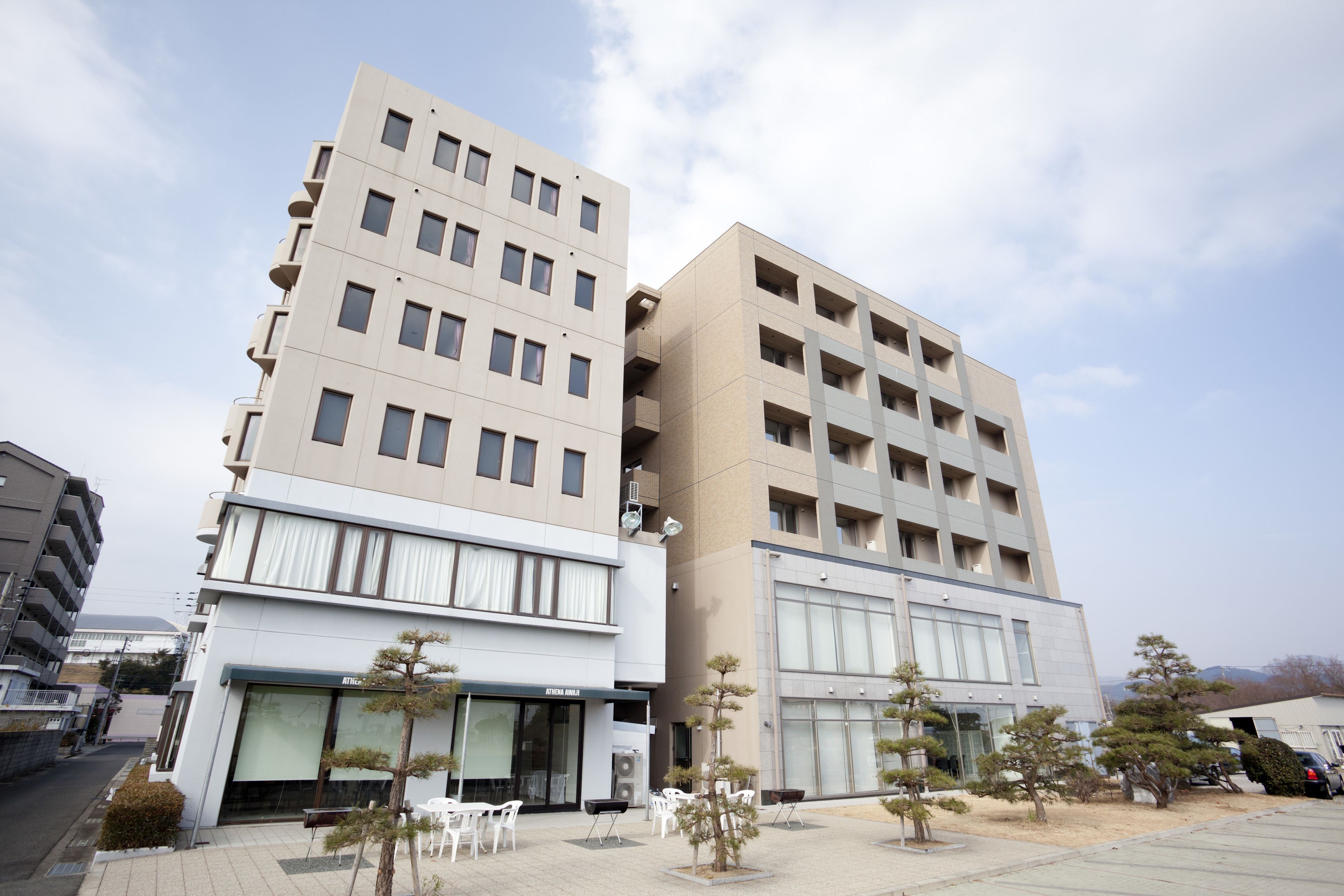 Un edifici modern amb diversos pisos, grans finestres i una zona de pàrquing amb arbres.